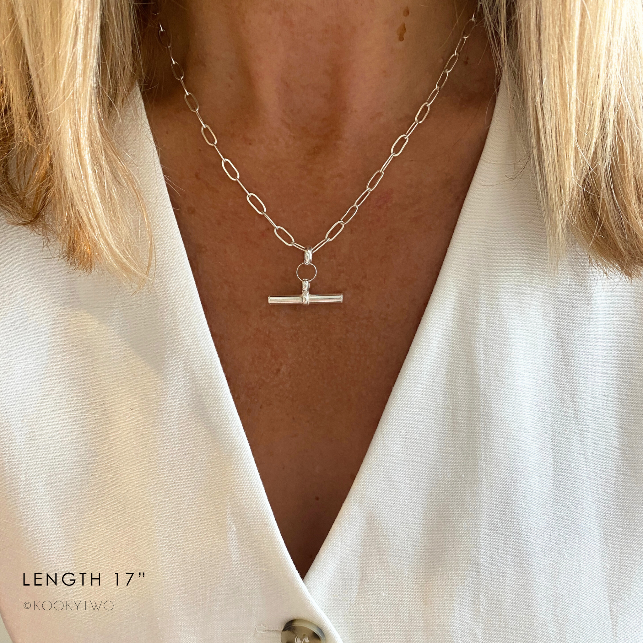 Silver necklace with t-bar charm worn by a person in white waistcoat.