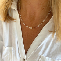 Person wearing a silver t-bar chain necklace with a white shirt