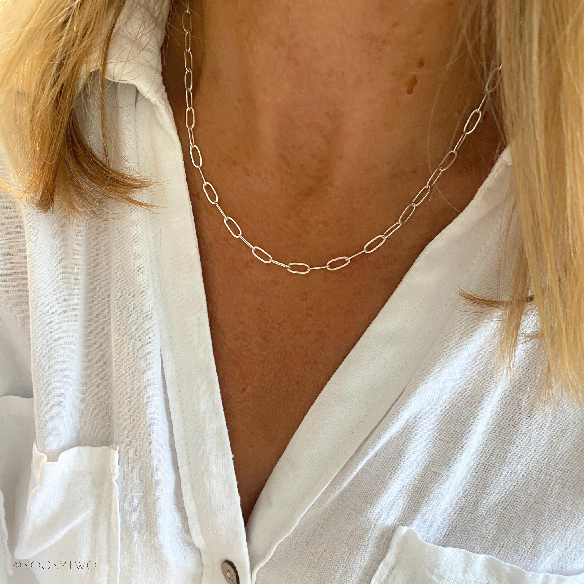 Person wearing a silver t-bar chain necklace with a white shirt