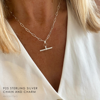 Silver chain necklace with a T-shaped charm worn by a person, wearing a white waistcoat.