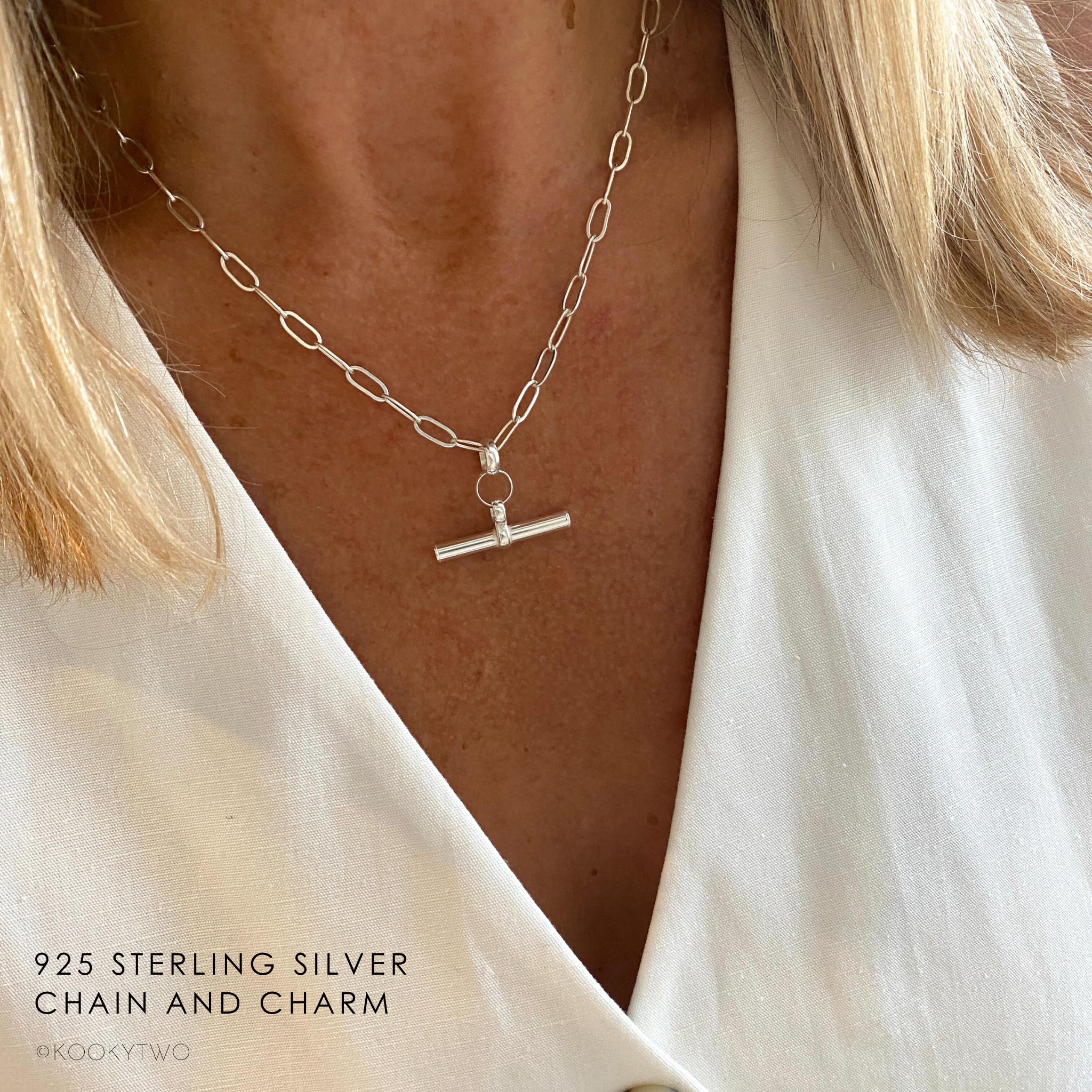 Silver chain necklace with a T-shaped charm worn by a person, wearing a white waistcoat.