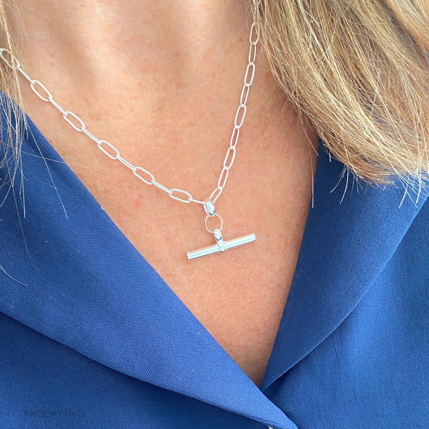 Silver chain necklace with a pendant on a person wearing a blue top.