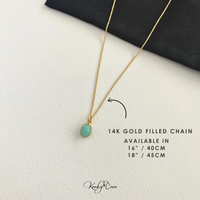 Gold necklace with a green pendant on a white surface, labeled '14K Gold Filled Chain'.
