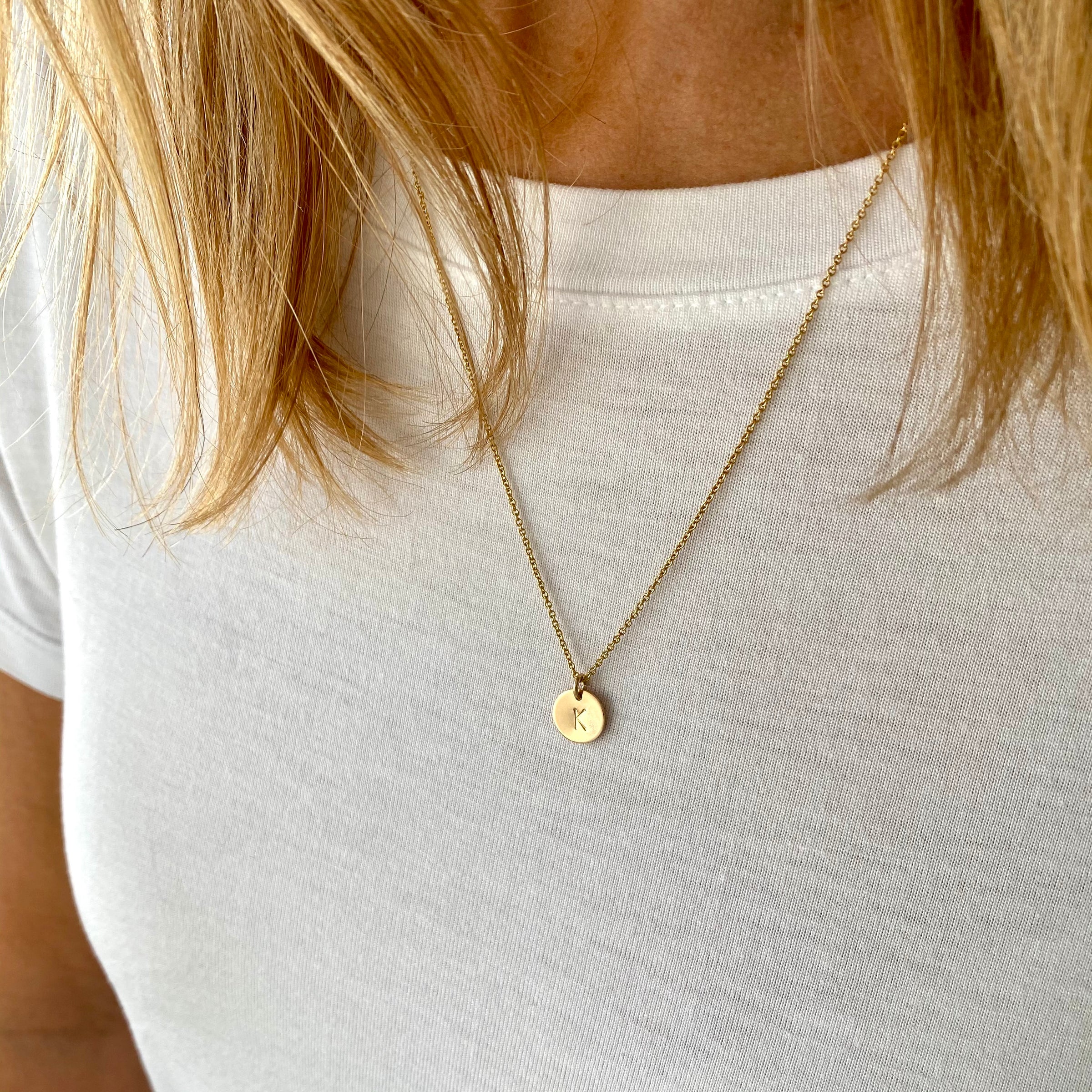A person wearing a white t-shirt with a gold initial disc necklace.