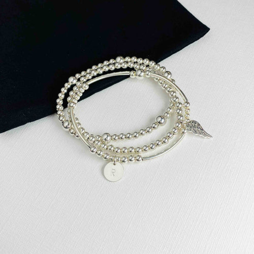 Silver stacking bracelet set with personalised disc and angel wing charm in silver. Personalised bracelet set with sterling silver bracelets and initial disc and angel wing charm. Hand beaded bracelet.
