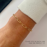Chunky gold chain bracelet on a wrist with text about clasp fitting each link meaning it's an adjustable bracelet.