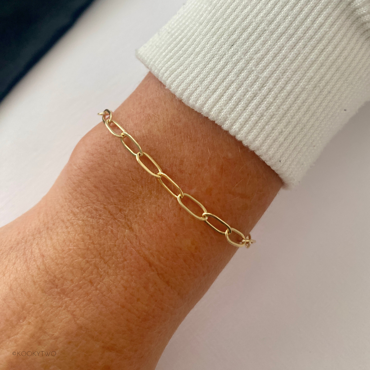 14k gold filled chain bracelet on a wrist with a neutral background