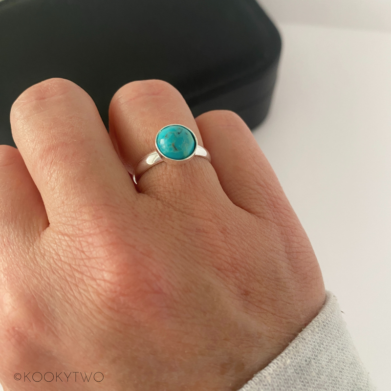 Turquoise ring on a person's finger with a neutral background
