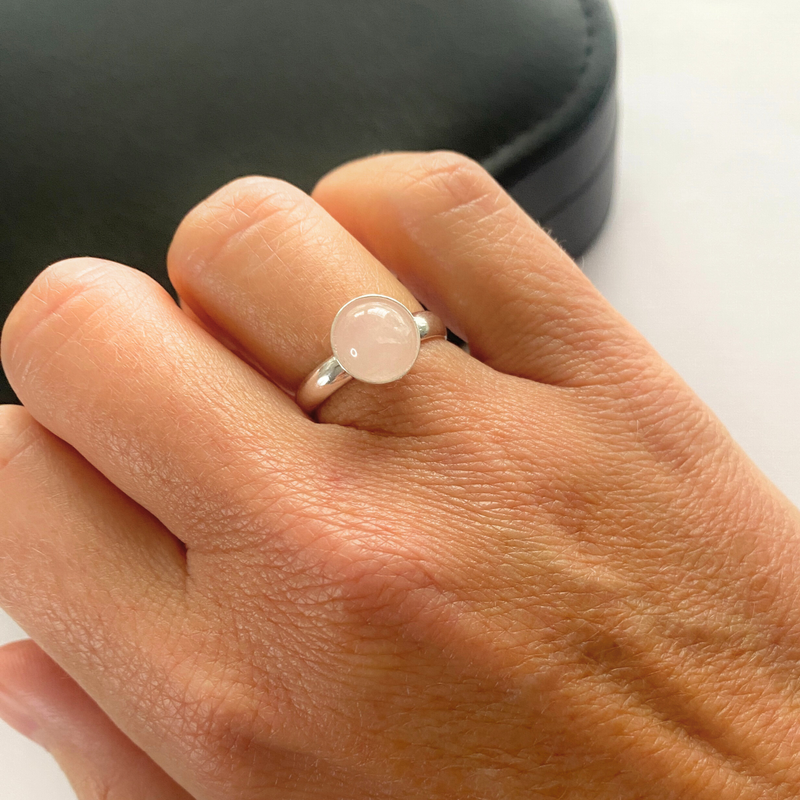 Hand wearing a sterling silver ring with a round pink gemstone on a neutral background. Gemstone is Rose Quartz on adjustable ring.