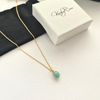 Gold necklace with amazonite pendant on a white surface next to a white gift box.