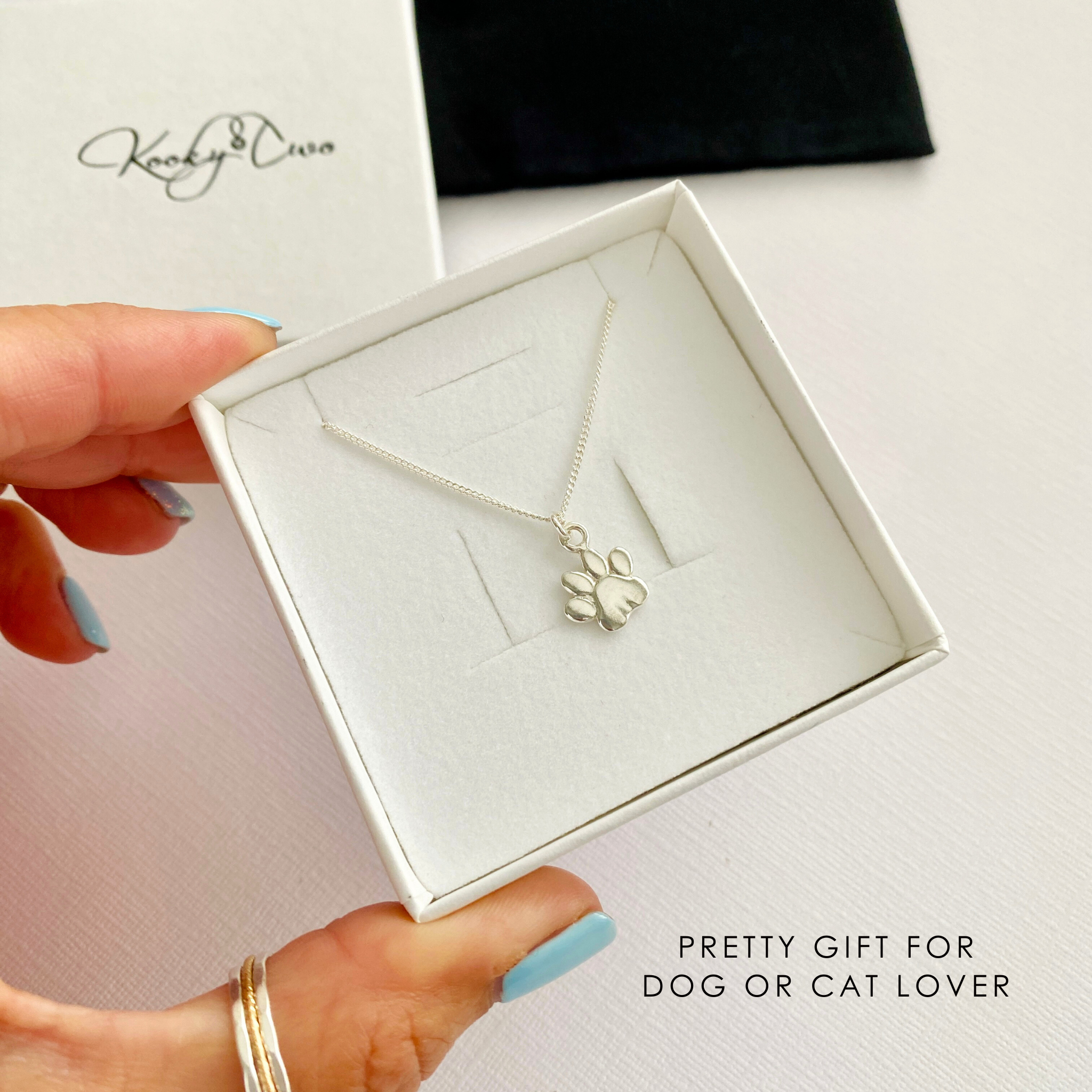 Sterling Silver paw print necklace in a white box held by a hand, with KookyTwo branding.