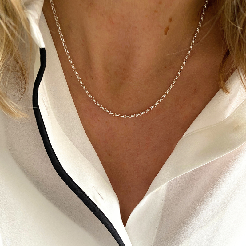 Silver belcher chain necklace worn by a person with a white blouse with black edging.