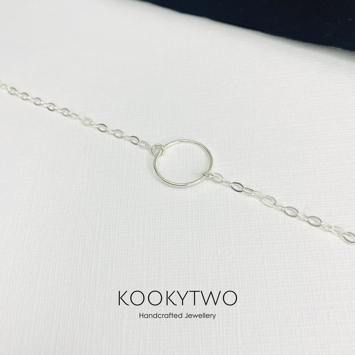 Silver necklace with a circular pendant on a white background, branded 'KOOKYTWO'.
