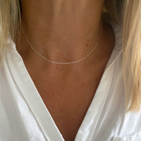 A close-up of a delicate sterling silver chain necklace worn on a woman's neck, paired with a white blouse.