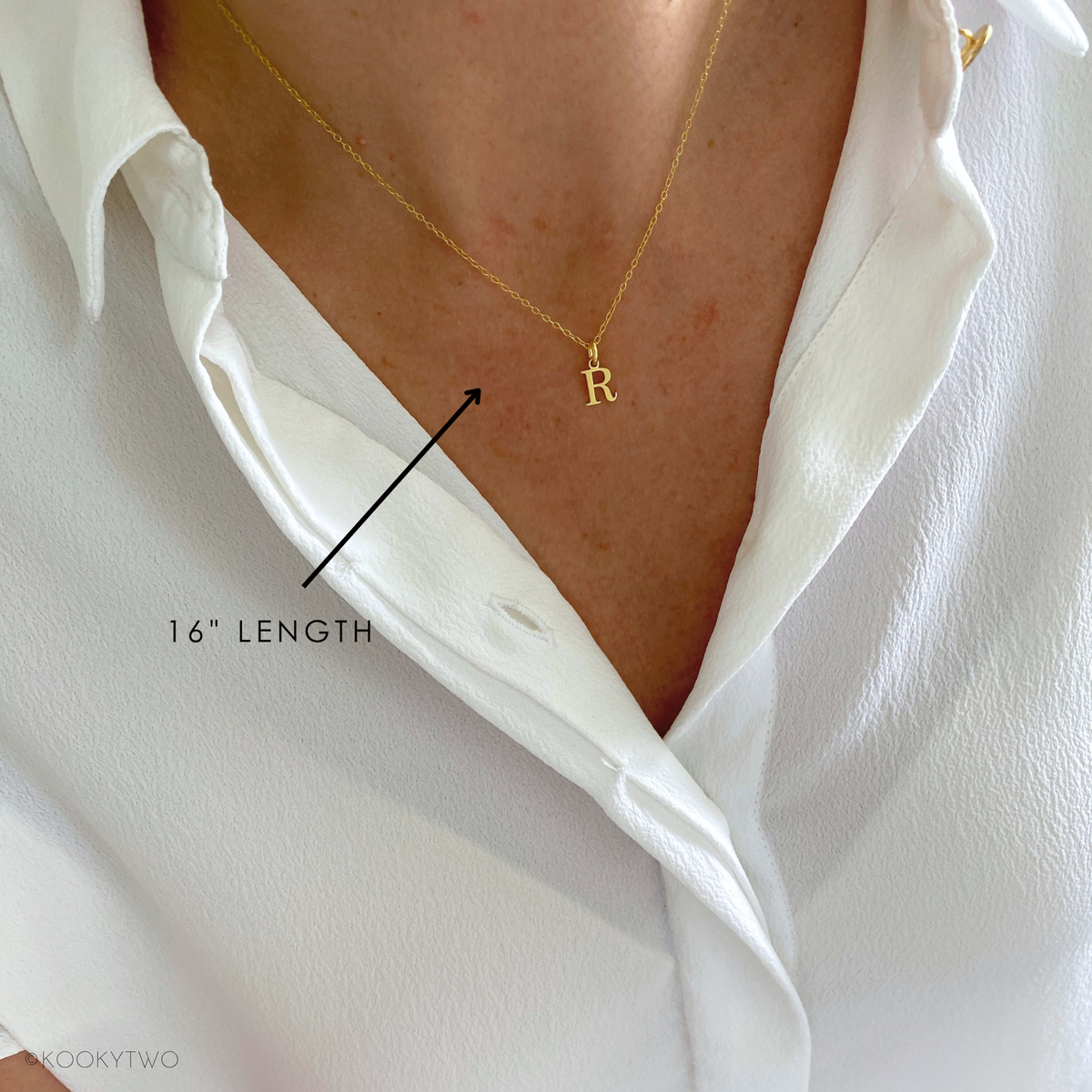 A close-up of a person wearing a delicate gold necklace with a small initial pendant, styled with a white shirt. A black arrow points to the necklace with the text '16" LENGTH' overlaid.