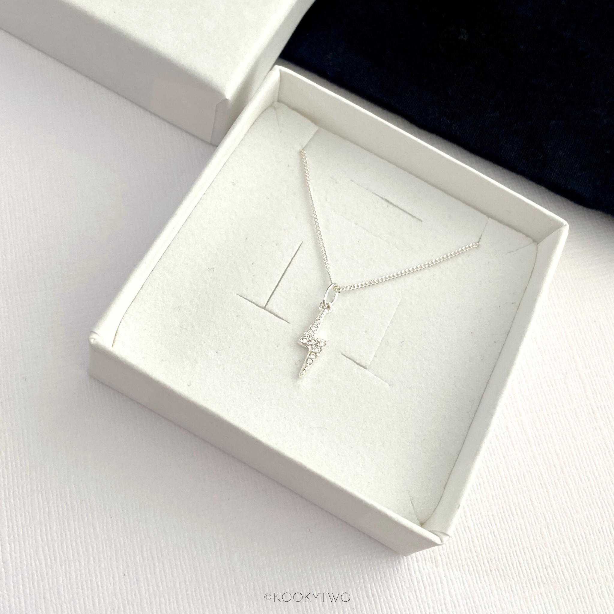 Sterling silver necklace with a crystal lightning bolt pendant in an open white jewellery box on a light surface.