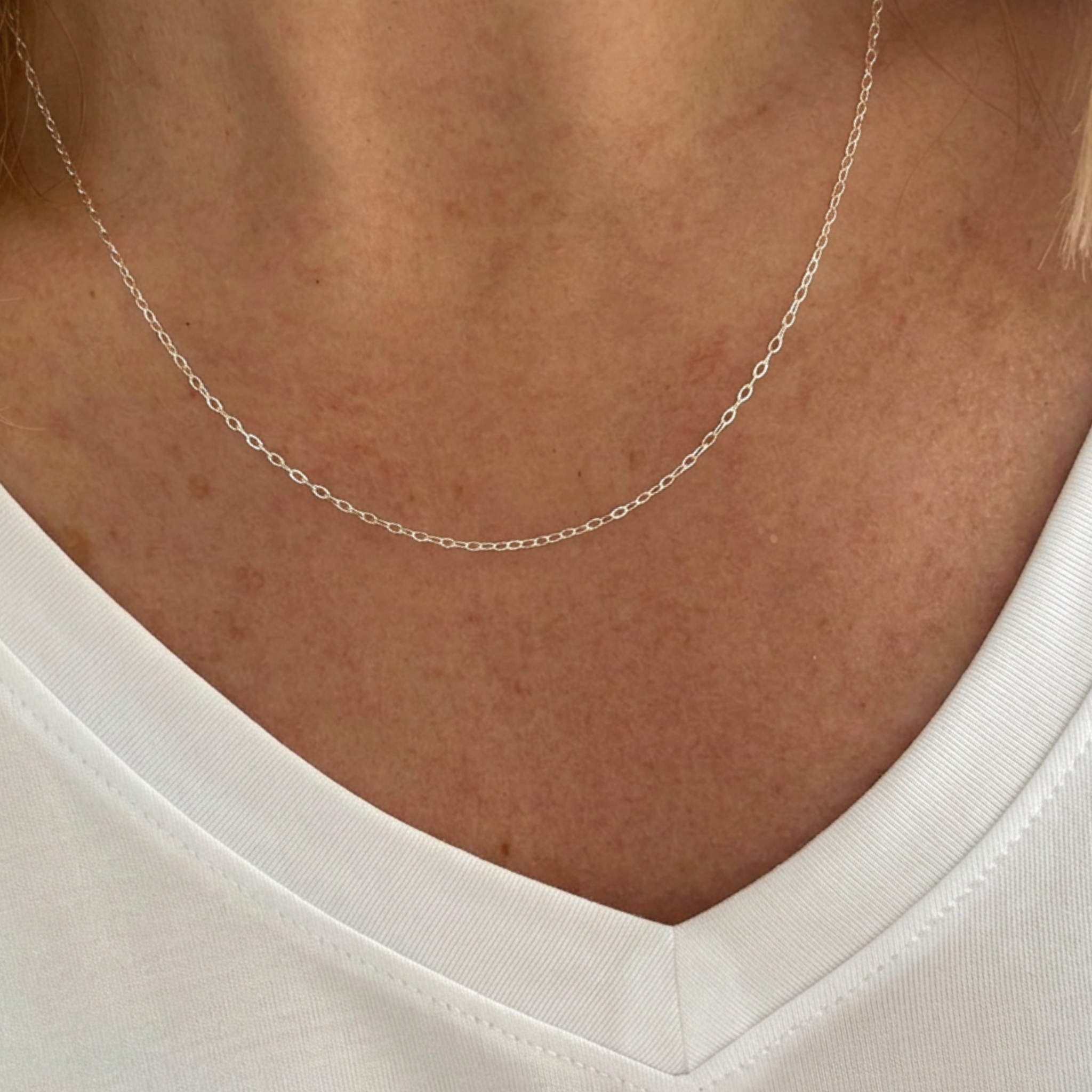 A close-up of a delicate silver chain necklace worn on a person's neck, paired with a white V-neck top.