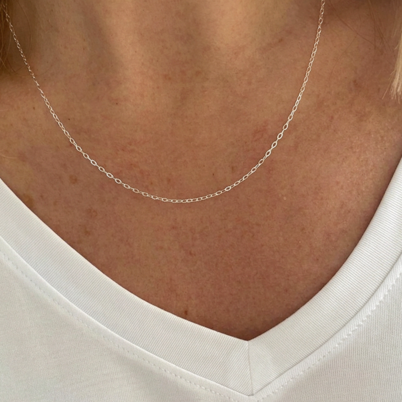 A close-up of a delicate silver chain necklace worn on a person's neck, paired with a white V-neck top.