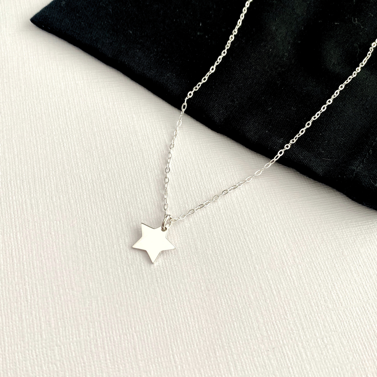 Silver star necklace on a white surface with black fabric background.