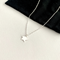 Silver star necklace on a white surface with black fabric background.