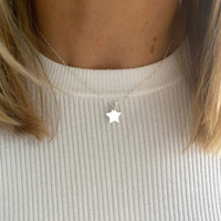 Short star necklace with star charm in sterling silver on a dainty silver chain. Worn on a person wearing a light-coloured top.