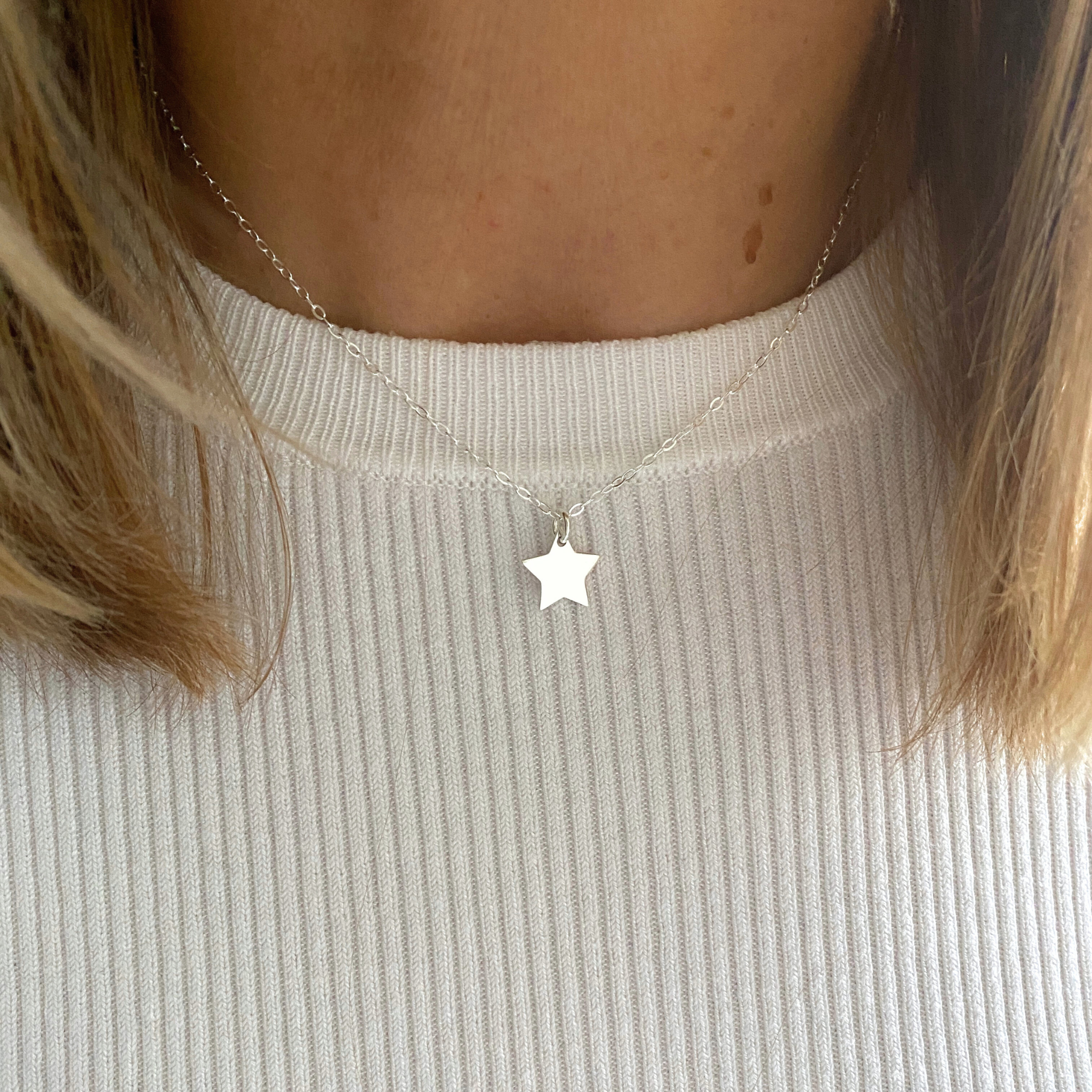 Short star necklace with star charm in sterling silver on a dainty silver chain. Worn on a person wearing a light-coloured top.