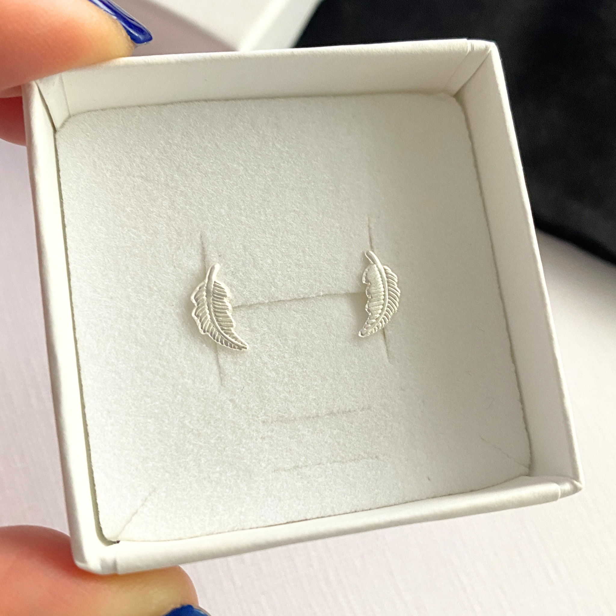 Silver feather earrings in a white box held by a hand.