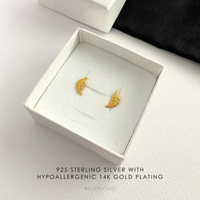 Gold feather earrings in a white box.
