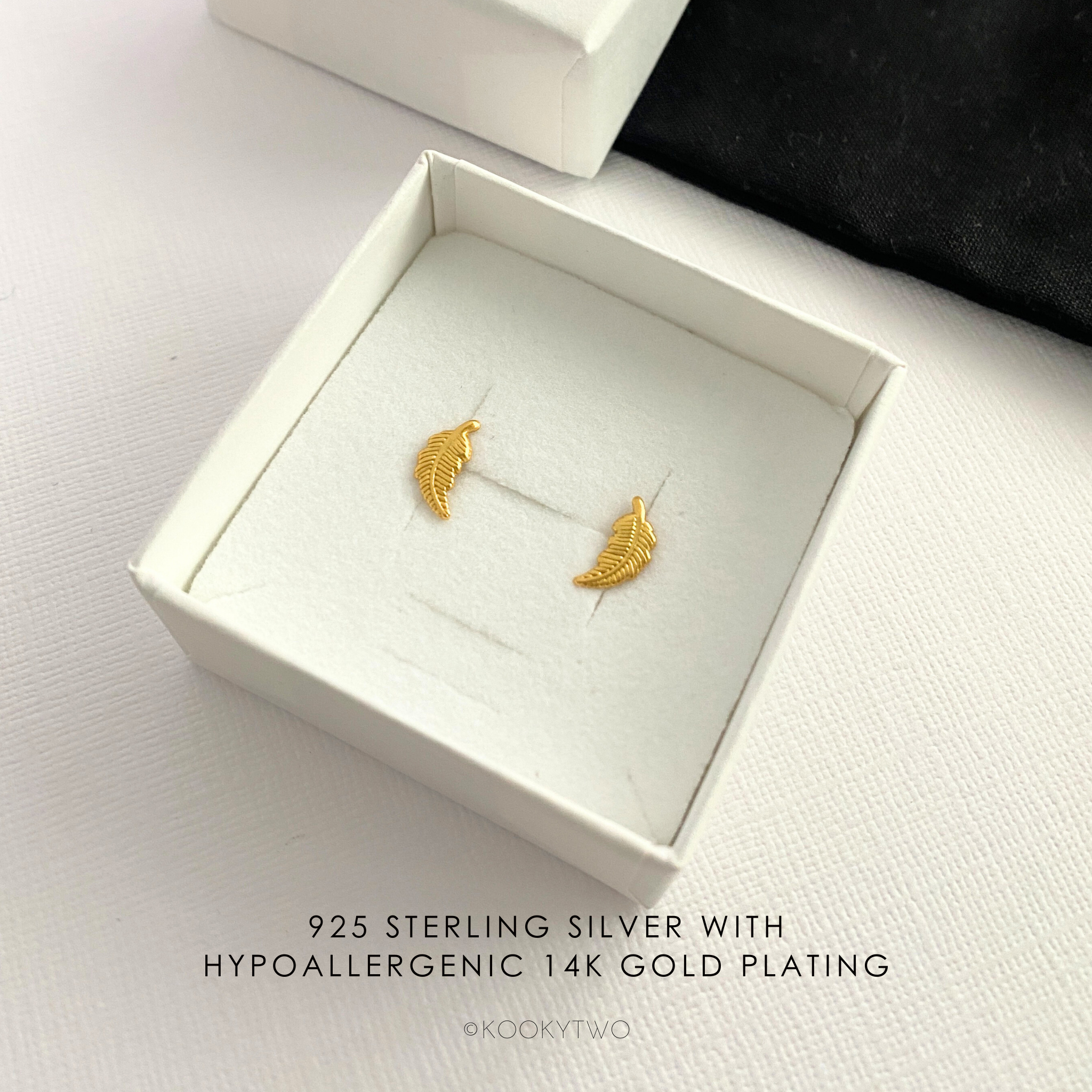 Gold feather earrings in a white box.