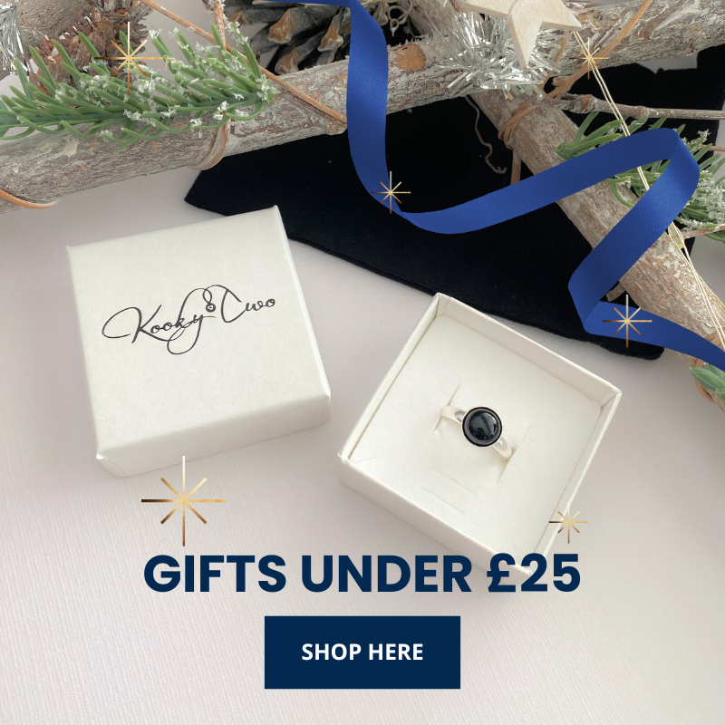 Open jewellery box with black onyx ring inside, KookyTwo brand visible, Christmas tree branches and blue ribbon in the background.