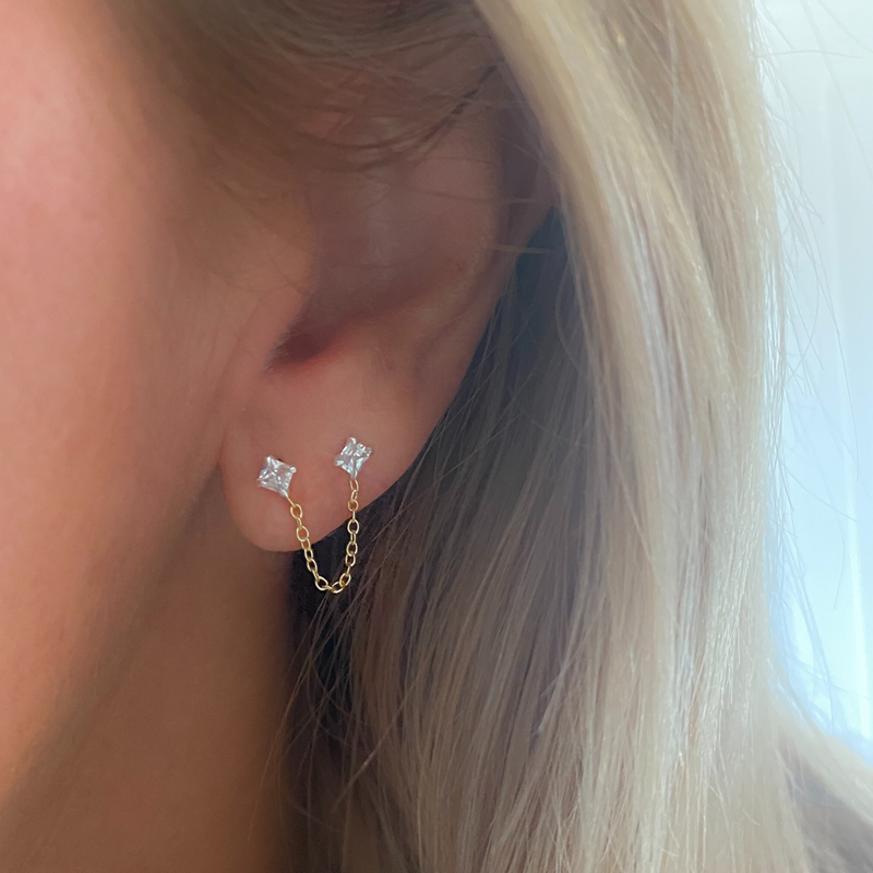 Ear showing gold and crystal ear jacket with chain between two crystal stones.