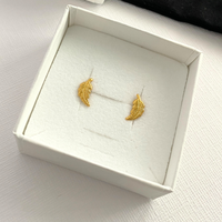 Gold feather-shaped earrings in a white box.