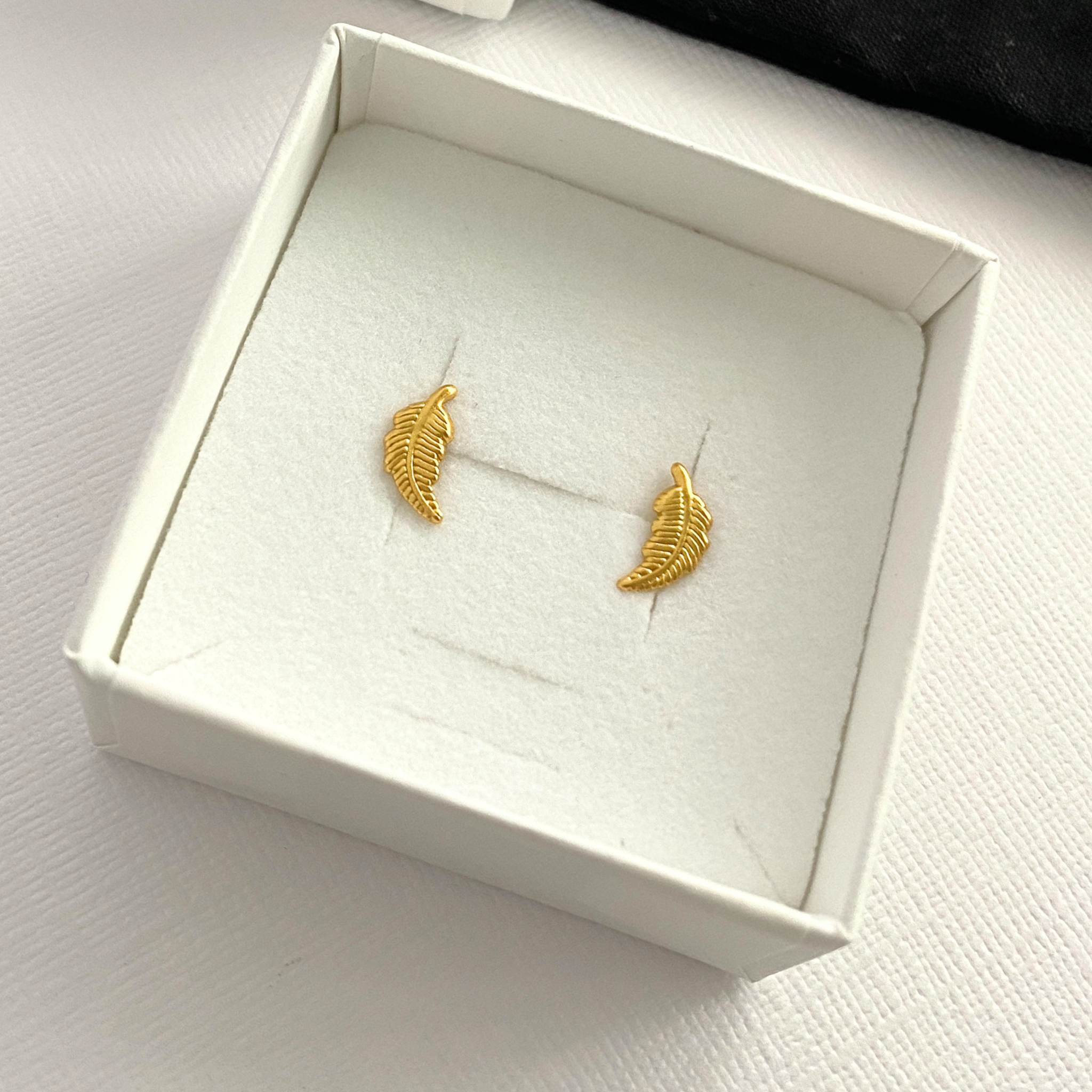 Gold feather-shaped earrings in a white box.