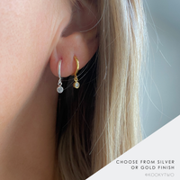 Close-up of a lady wearing two hoop earrings, one silver and one gold, with a sparkly crystal charm.
