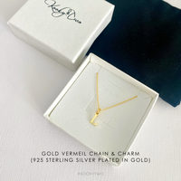 A gold vermeil chain necklace with a small letter pendant, displayed inside an open white jewellery box. The brand box lid with 'KookyTwo' logo is visible in the upper left, and a dark velvet pouch is on the right.