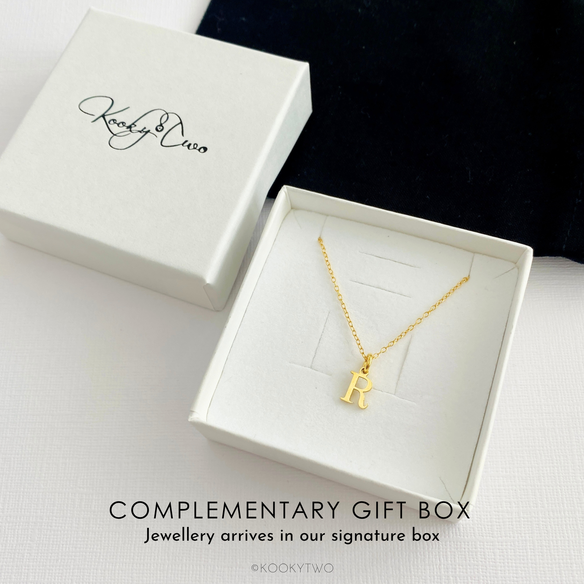 A gold vermeil initial necklace with the letter 'R' pendant displayed in an open white jewellery gift box, with the matching closed box beside it on a white surface. The brand name 'Kookytwo' is printed on the box lid, and text at the bottom reads 'COMPLEMENTARY GIFT BOX' and 'Jewellery arrives in our signature box'.