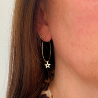 A close-up of a person's ear wearing a delicate gold hoop earring with a dangling star charm and a small gold stud earring.