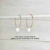Gold hoop earrings with star charms on a light wooden background