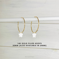 Gold hoop earrings with star charms on a light wooden background