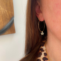 Person wearing a 14k gold filled hoop earring with a gold star charm, paired with a leopard-print top.