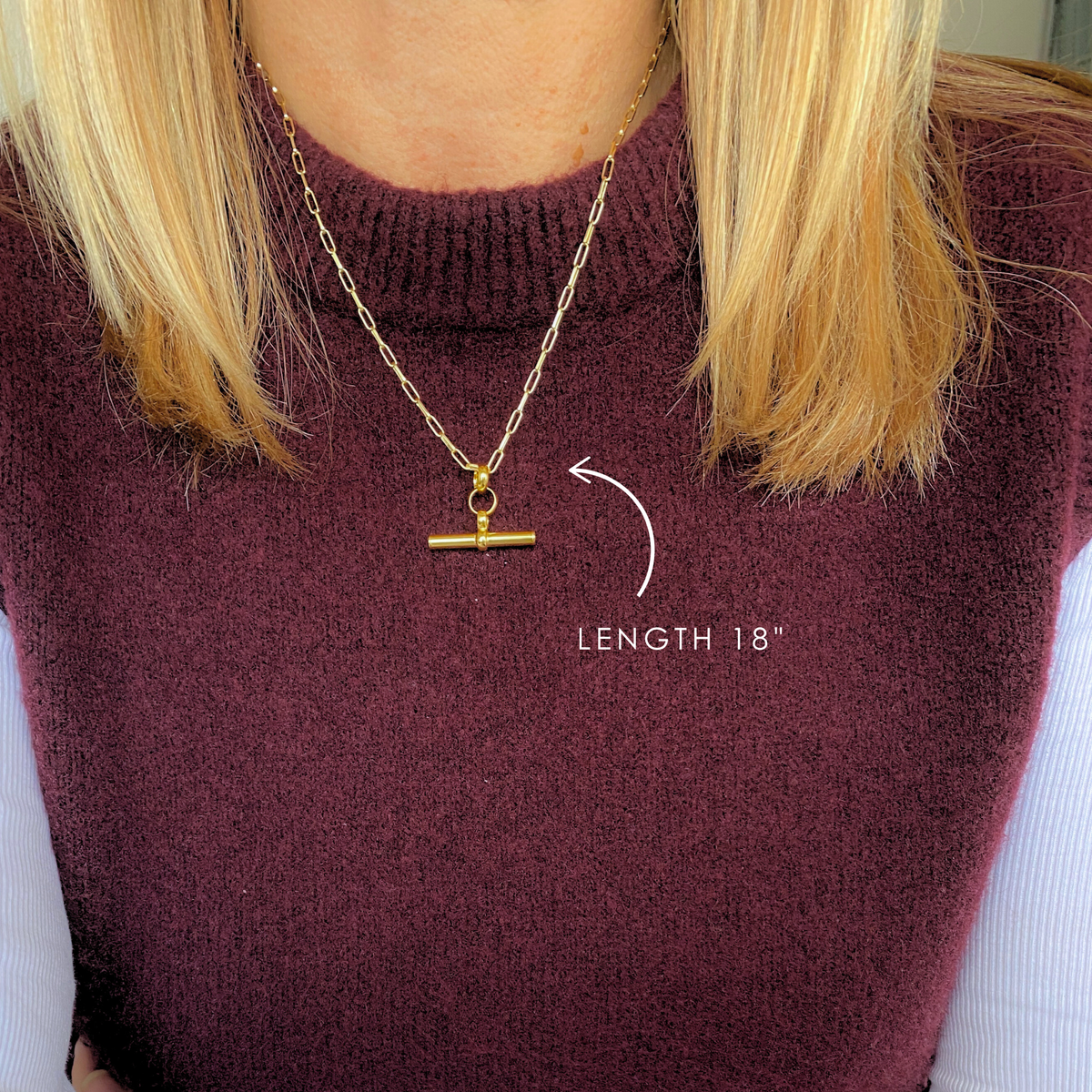 A bold and stylish eye-catching gold t bar necklace. A modern and elegant statement necklace, perfect for everyday wear. T Bar necklace shown worn over on-trend burgundy top.
