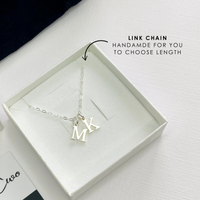 Silver necklace with 'K' and 'M' charms in a box on a white background