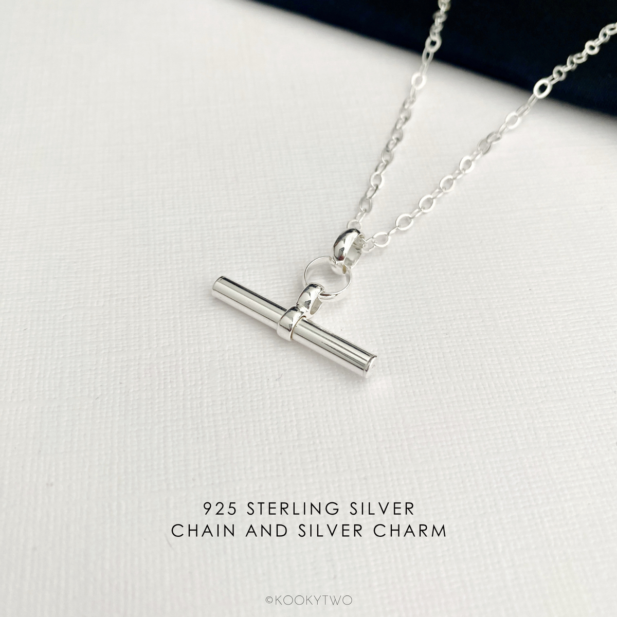 925 Sterling silver necklace with a simple plain t bar charm on a silver chain, displayed on a textured white surface with text overlay '925 STERLING SILVER CHAIN AND SILVER CHARM'.