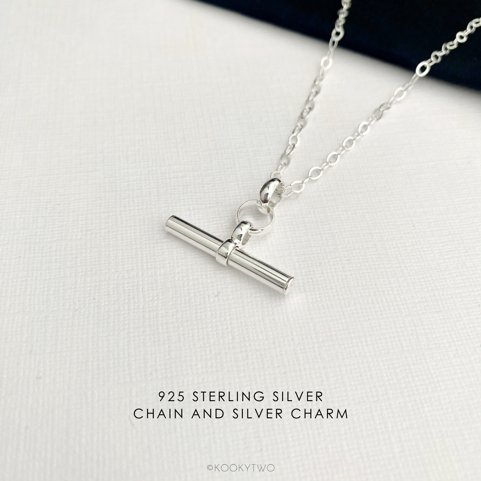 925 Sterling silver necklace with a simple plain t bar charm on a silver chain, displayed on a textured white surface with text overlay '925 STERLING SILVER CHAIN AND SILVER CHARM'.