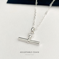 A silver adjustable t bar necklace on a textured white surface, with a dark navy velvet box corner visible in the background. The text 'ADJUSTABLE CHAIN' and the brand name 'KOOKYTWO' are printed at the bottom.