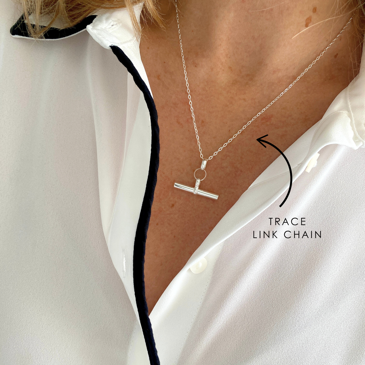 Silver t-bar necklace with a trace link chain worn by a person, with a close-up view.
