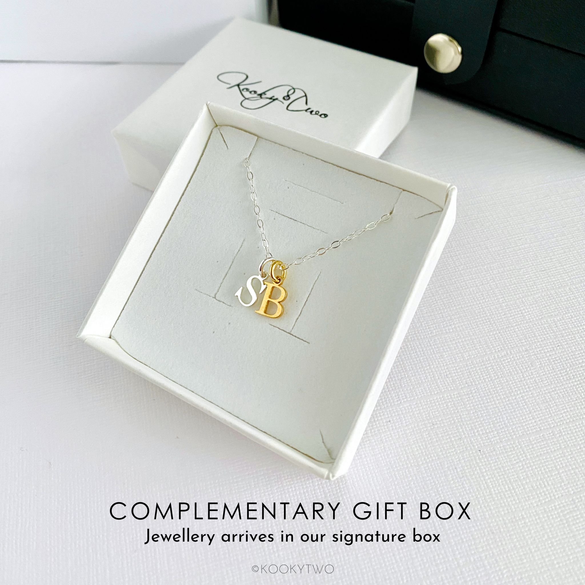 Mixed metal silver and gold necklace with capital letter pendants in a white gift box on a white background.