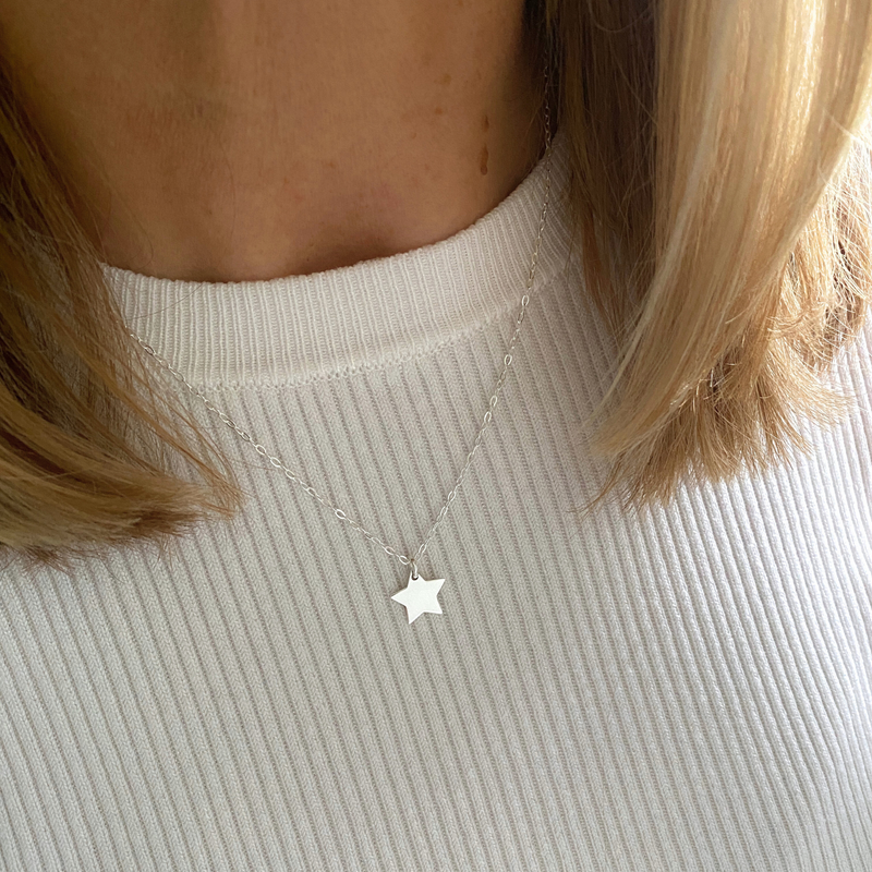 Star charm necklace worn by a person with light skin and blonde hair, with cream jumper.