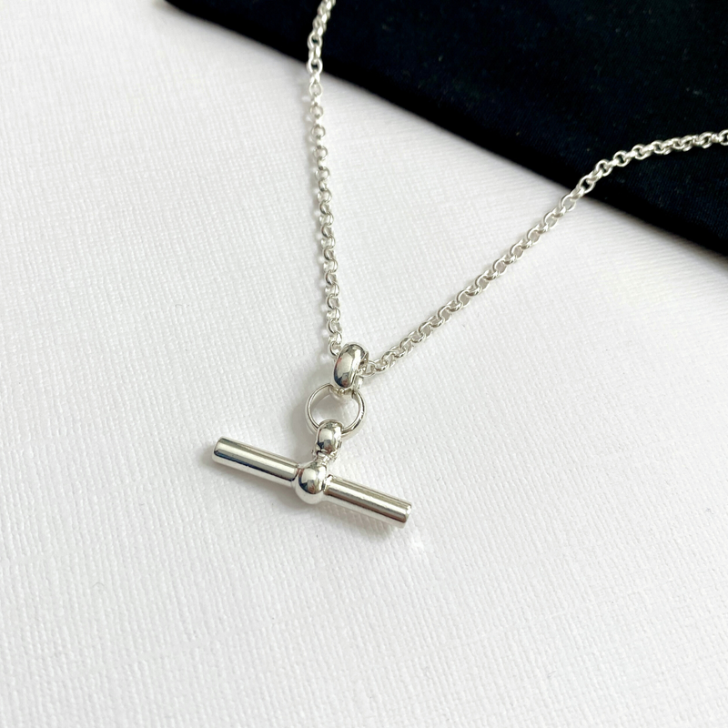 Close-up of hanging T-bar charm necklace, showing its sleek and polished design, handmade with sterling silver belcher chain. KookyTwo.