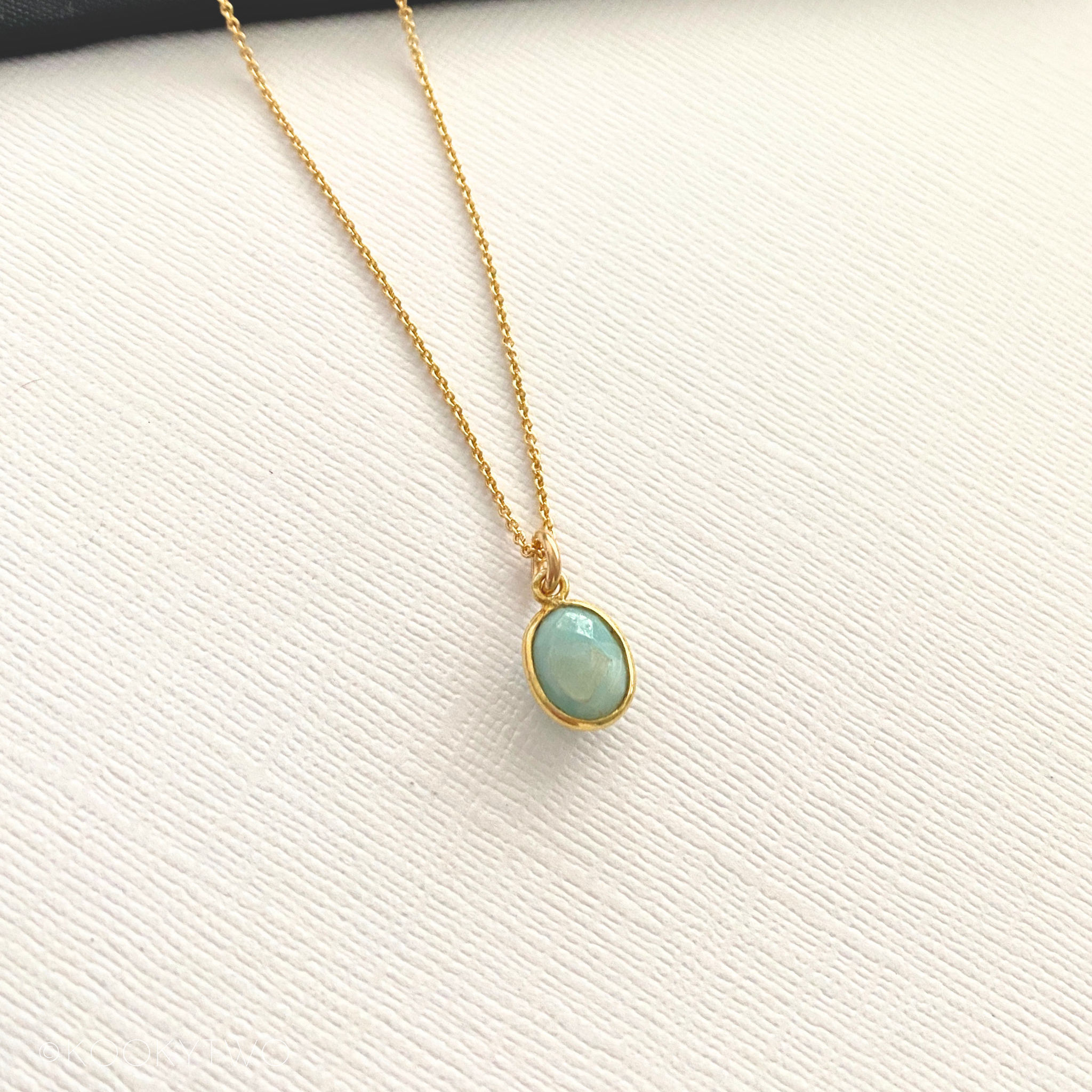 Gold necklace with a pale blue pendant on a white background